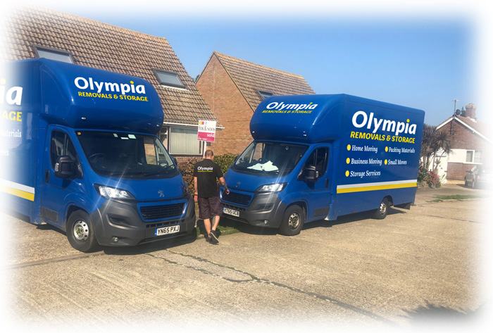 Two blue Olympia Removals & Storage vans parked outside a house with a mover between them